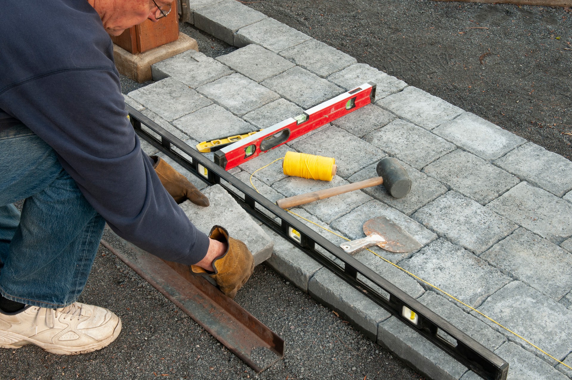 Worker laying paving bricks with tools and a level on ground
