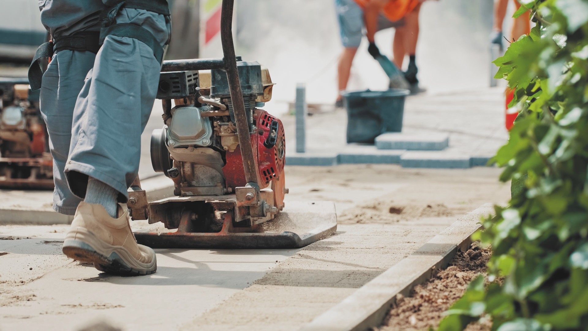 Roadworks Construction Worker Using Ground Plate Compactor Preparing Surface for Laying Sidewalk Pavement Flagstones