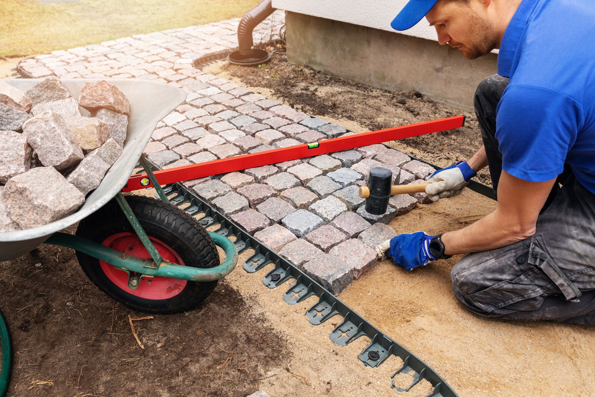 worker laying granite cobblestone pathway around the house