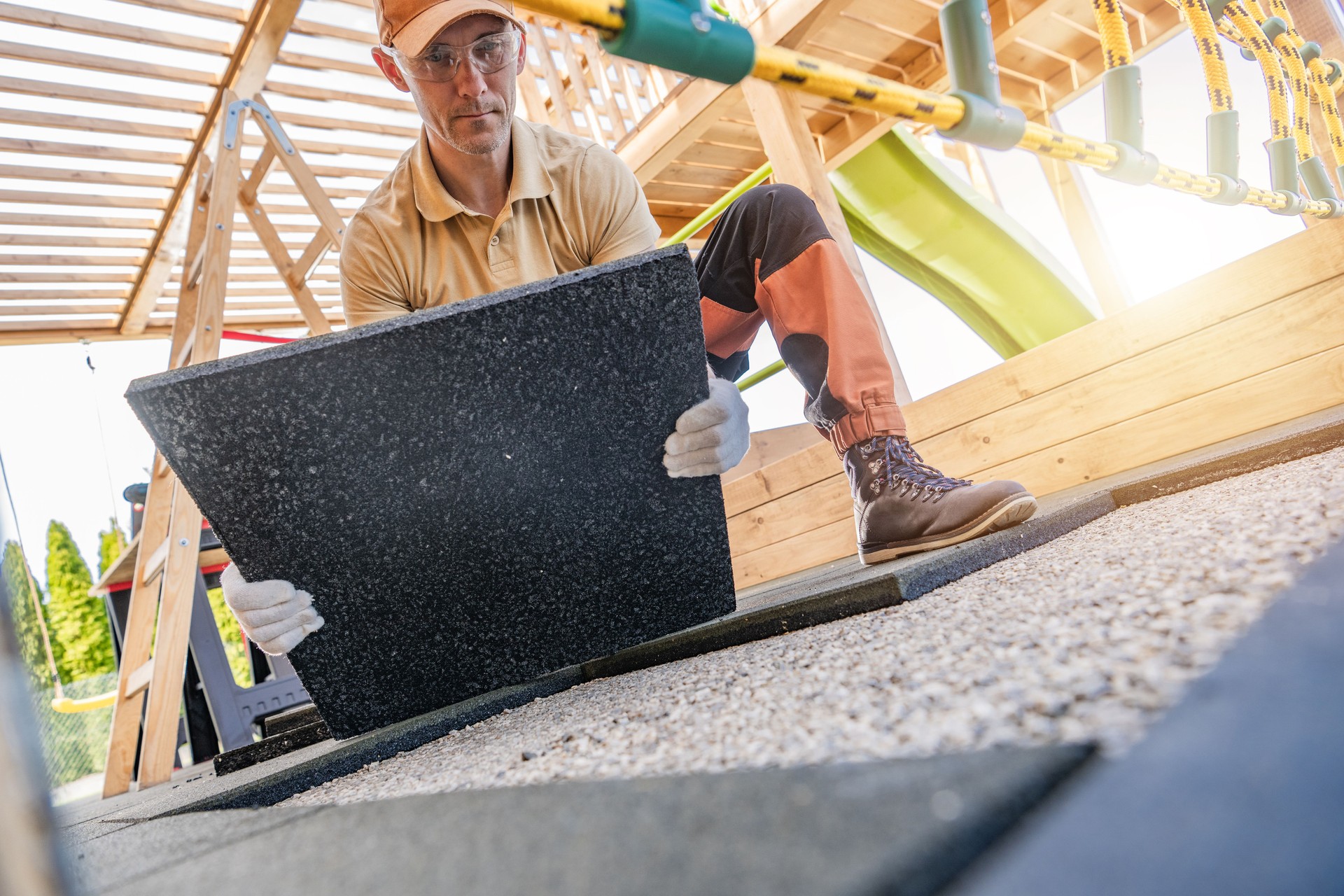 Worker Laying Down Rubber Tiles in a Playground Renovation Project During a Sunny Afternoon in a Suburban Area